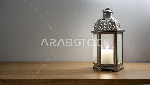 ديكورات وأنوار في الأجواء الرمضانية الروحانية، صورة مقربة لفانوس معدني مزخرف مضيء على طاولة خشبية، تحف اسلامية تقليدية للاحتفال بقدوم شهر الخير، زينة رمضان المبارك على الطراز الاسلامي