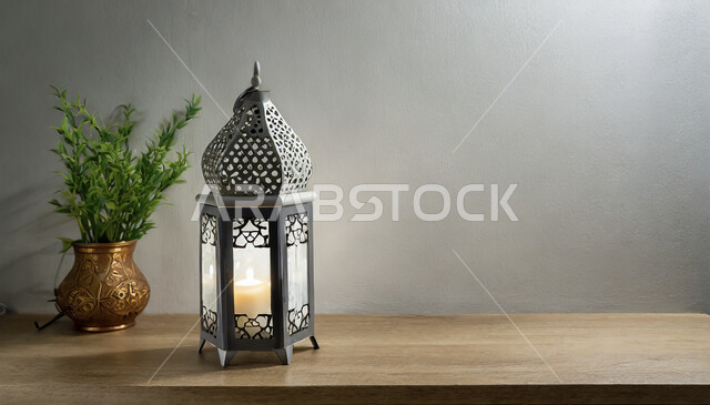 ديكورات وأنوار في الأجواء الرمضانية الروحانية، صورة مقربة لفانوس معدني مزخرف مضيء على طاولة خشبية، تحف اسلامية تقليدية للاحتفال بقدوم شهر الخير، زينة رمضان المبارك على الطراز الاسلامي