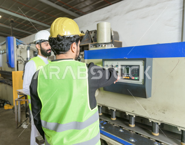 مهندسان  سعوديان عاملان يشرفان في داخل المصنع في المملكة العربية السعودية , إرتداء خوذة وسترة الحماية الخاصة بالعمل , العامل المسؤول بخوذة صفراء , المهندس المشرف بخوذة بيضاء , فحص المعدات بأنفسهم , تدقيق العمل , الإشراف والنقاش في العمل