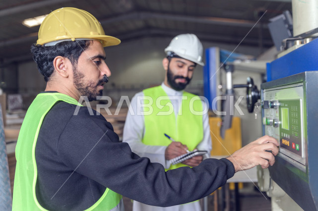 مهندسان  سعوديان عاملان يشرفان في داخل المصنع في المملكة العربية السعودية , إرتداء خوذة وسترة الحماية الخاصة بالعمل , العامل المسؤول بخوذة صفراء , المهندس المشرف بخوذة بيضاء , فحص المعدات بأنفسهم , تدقيق العمل , الإشراف والنقاش في العمل