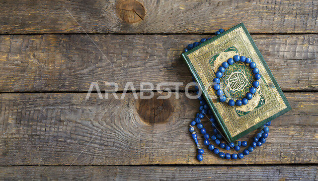 صورة علوية عامودية للمصحف الشريف بجانب سبحه مصنوعه من الخرز لذكر الله تعالى على لوح خشبي, التعبد والاجتهاد بالطاعة بتلاوة القران و ذكر الله, الهداية بنور القرآن الكريم, حفظ و تفسير آيات الكتاب الشريف