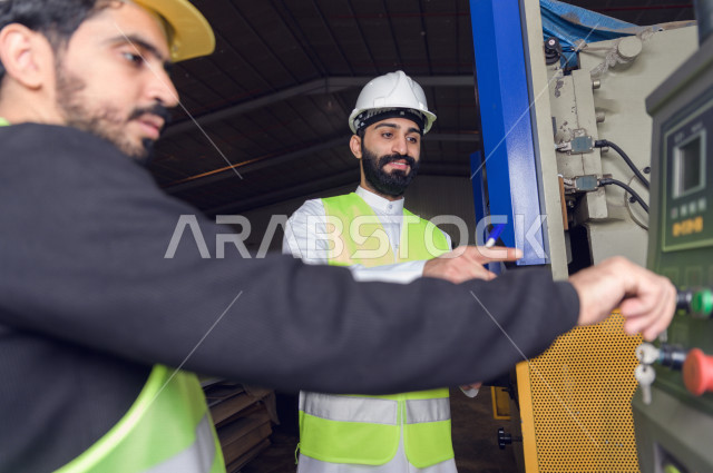 مهندسان  سعوديان عاملان يشرفان في داخل المصنع في المملكة العربية السعودية , إرتداء خوذة وسترة الحماية الخاصة بالعمل , العامل المسؤول بخوذة صفراء , المهندس المشرف بخوذة بيضاء , فحص المعدات بأنفسهم , تدقيق العمل , الإشراف والنقاش في العمل