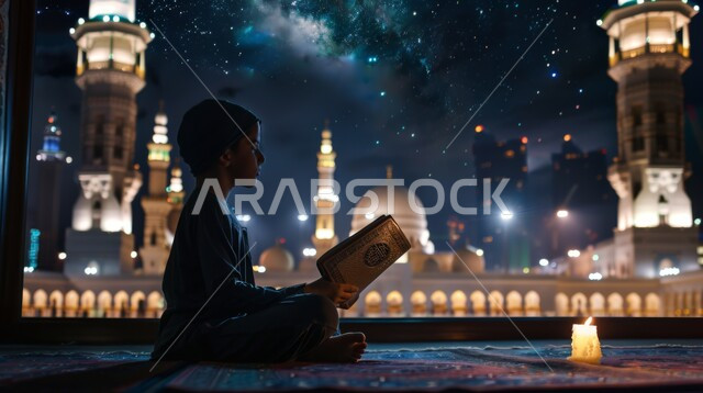 الجلسات الإسلامية الروحانية الهادئة في شهر رمضان المبارك، زرع الفطرة السليمة الصحيحة في الأبناء، تلاوة وقراءة القرآن الكريم، الإكثار من الطاعة والتقرب الى الله، ولد عربي خليجي سعودي يحمل بيده المصحف الشريف يجلس أمام واجهه مطلة على أحد المساجد الاسلامية