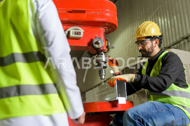 عامل مسؤول ومشرف سعودي يرتدي خوذه صفراء يشرف داخل المصنع في المملكة العربية السعودية , ارتداء خوذة وسترة الحماية الخاصة بالعمل , التصنيع والإشراف والتدقيق في العمل , الهندسة والصناعة