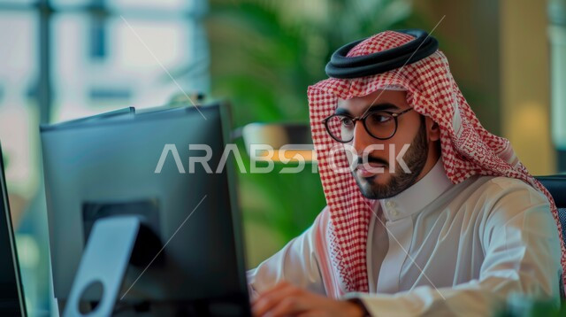  بيئة العمل المريحة في الشركات السعودية مفهوم إدارة شؤون الأعمال وتنظيمها عبر الاجهزة التقنية، مهن ووظائف ادارية مكتبية، صورة مقربة لرجل أعمال عربي خليجي سعودي يرتدي الزي التقليدي و النظارات الطبية يقوم باستخدام جهاز الحاسوب المحمول ضمن مقر الشركة