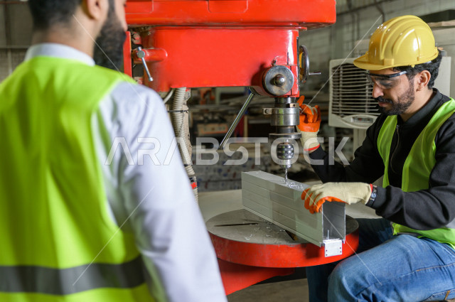 مهندسان  سعوديان عاملان يشرفان في داخل المصنع في المملكة العربية السعودية , إرتداء خوذة وسترة الحماية الخاصة بالعمل , العامل المسؤول بخوذة صفراء , المهندس المشرف بخوذة بيضاء , فحص المعدات بأنفسهم , تدقيق العمل , الإشراف والنقاش في العمل