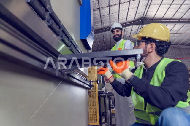 مهندسان  سعوديان عاملان يشرفان في داخل المصنع في المملكة العربية السعودية , إرتداء خوذة وسترة الحماية الخاصة بالعمل , العامل المسؤول بخوذة صفراء , المهندس المشرف بخوذة بيضاء , فحص المعدات بأنفسهم , تدقيق العمل , الإشراف والنقاش في العمل