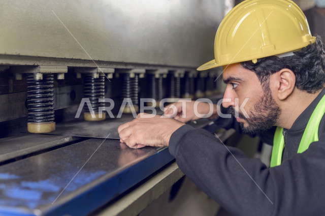 عامل مسؤول ومشرف سعودي يرتدي خوذه صفراء يشرف داخل المصنع في المملكة العربية السعودية , ارتداء خوذة وسترة الحماية الخاصة بالعمل , التصنيع والإشراف والتدقيق في العمل , الهندسة والصناعة