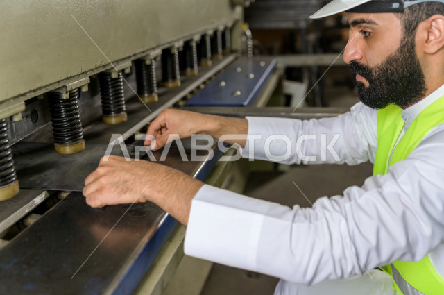 مهندس ومشرف سعودي يرتدي خوذه بيضاء يشرف داخل المصنع في المملكة العربية السعودية , ارتداء خوذة وسترة الحماية الخاصة بالعمل , التصنيع والإشراف والتدقيق في العمل , الهندسة والصناعة