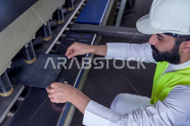 مهندس ومشرف سعودي يرتدي خوذه بيضاء يشرف داخل المصنع في المملكة العربية السعودية , ارتداء خوذة وسترة الحماية الخاصة بالعمل , التصنيع والإشراف والتدقيق في العمل , الهندسة والصناعة