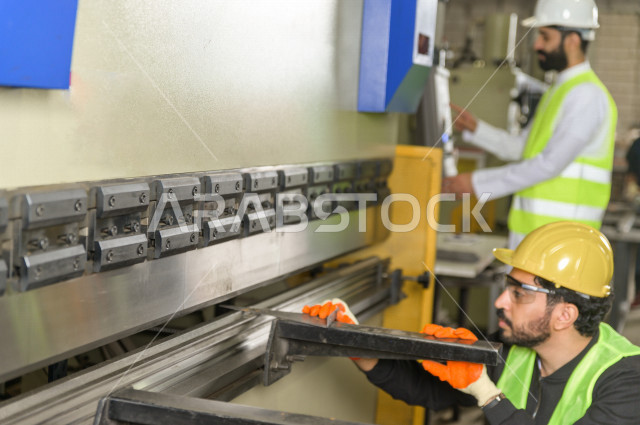 مهندسان  سعوديان عاملان يشرفان في داخل المصنع في المملكة العربية السعودية , إرتداء خوذة وسترة الحماية الخاصة بالعمل , العامل المسؤول بخوذة صفراء , المهندس المشرف بخوذة بيضاء , فحص المعدات بأنفسهم , تدقيق العمل , الإشراف والنقاش في العمل