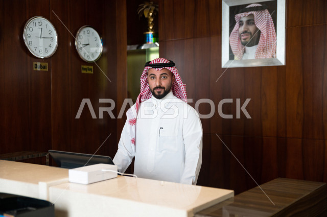 موظف إستقبال خليجي سعودي يرحب بالزوار داخل الفندق بإيماءات وجه ويدين مختلفة , رجل بشوش الوجه يرتدي ثوب أبيض مع شماغ عقال , سياحة وفندقة , مكتب إستقبال العملاء 