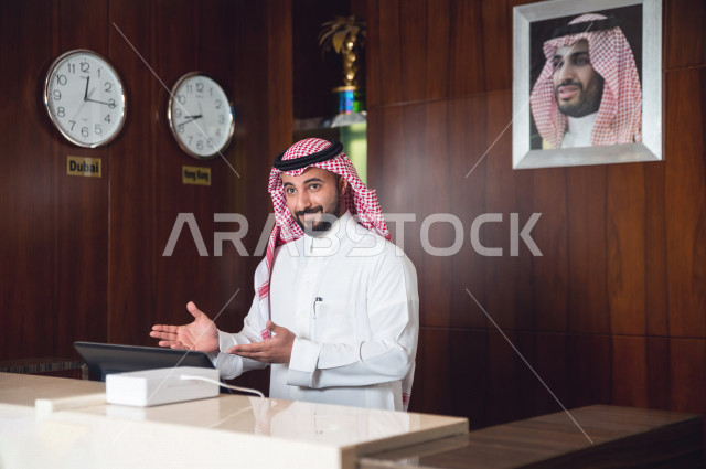 موظف إستقبال خليجي سعودي يرحب بالزوار داخل الفندق بإيماءات وجه ويدين مختلفة , رجل بشوش الوجه يرتدي ثوب أبيض مع شماغ عقال , سياحة وفندقة , مكتب إستقبال العملاء 
