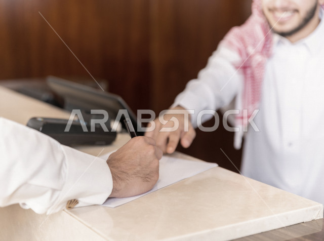 صورة مقربة لسائح خليجي سعودي يقوم بإجراءات الحجز والدخول لدى مكتب الاستقبال في الفندق , سياحة وفندقة 