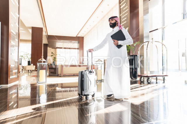 رجل أعمال خليجي سعودي يجر حقيبة سفر عند مدخل الفندق من الداخل , سياحة وفندقة , قضاء أوقات ممتعة , رحلة عمل