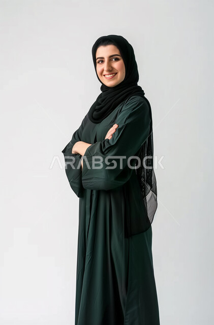الملامح العربية القوية، النظر الى الكاميرا بإيماءات البهجة والسرور، مفهوم الأنوثة والنعومة، أزياء محجبات عصرية وأنيقة، الاهتمام بالمظهر الخارجي، بورتريه لشابة عربية خليجية سعودية ترتدي العباية والحجاب تقف بأيدي متقاطعة، خلفية رمادية