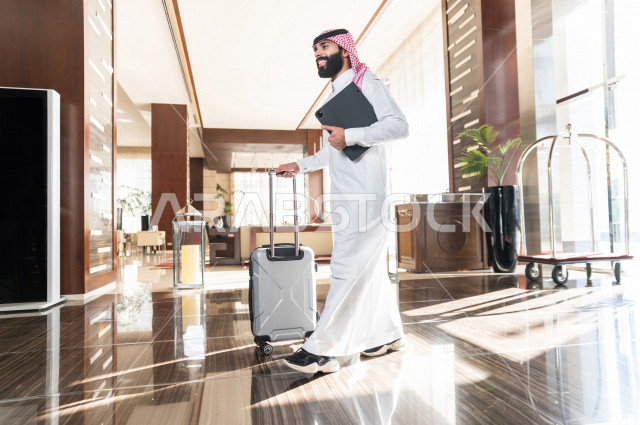 رجل أعمال خليجي سعودي يجر حقيبة سفر عند مدخل الفندق من الداخل , سياحة وفندقة , قضاء أوقات ممتعة , رحلة عمل