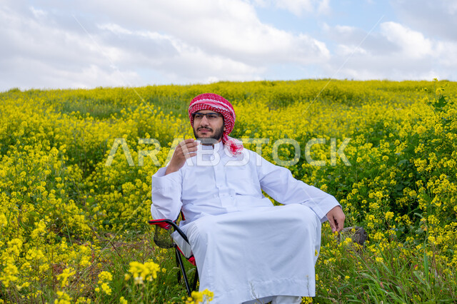 Hiking in the farms of Saudi Arabia, enjoying the natural scenery in the spring, breathing fresh air during the day, a young Saudi Arabian Gulf man wearing a traditional shemagh and thobe sitting on a chair holding a cup of coffee in his hand, gestures and expressions of pleasure and happiness, nature background