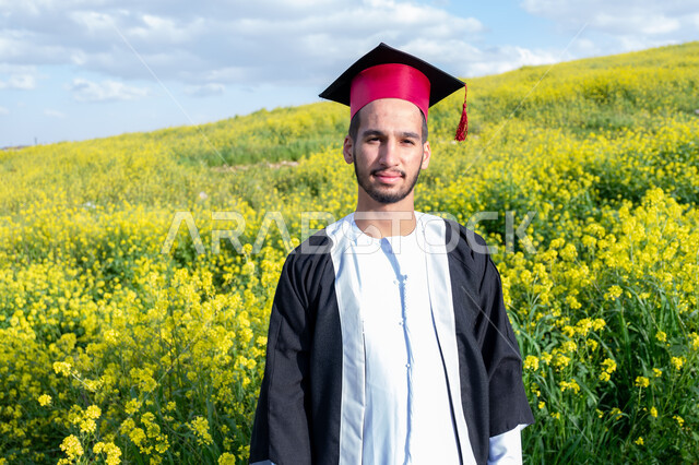 تحقيق حلم النجاح من الجامعة، المنتزهات الطبيعية في الامارات، الاحتفال بيوم التخرج بإيماءات السعادة والحماس، صورة مقربة لشاب عربي خليجي إماراتي مبتسم يرتدي الكندورة وزي التخرج مع القبعة في الخارج، الاستمتاع بالمناظر الطبيعية في فصل الربيع، خلفية الطبيعة