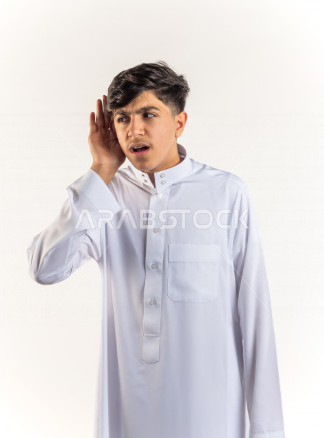 بورتريه ولد خليجي سعودي يضع يده على أذنه بإيماءات وجه ويدين مختلفة , خلفية بيضاء