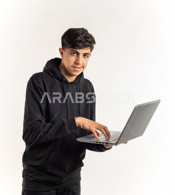 بورتريه شاب مراهق خليجي سعودي يستخدم الابتوب ، يتابع حصص الاونلاين عن طريق الحاسوب المحمول ، التعلم عن بعد ، مفهوم التعليم عبر الانترنت ، التعليم المنزلي ، خلفية بيضاء