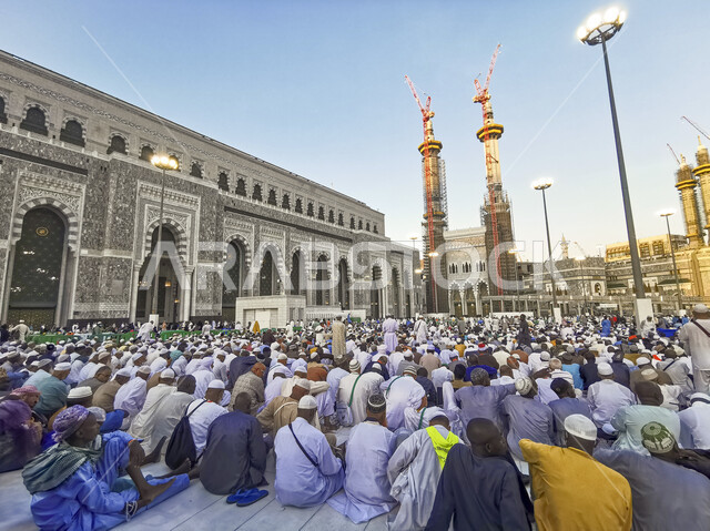 معالم وأماكن دينية إسلامية مقدسة، الحجاج والمعتمرين يجلسون في الفناء الخارجي لمسجد الحرام، أداء مناسك الحج والعمرة، الفن الهندسي المعماري للأبراج المطلة على ساحات الحرم المكي الشريف في مكة المكرمة في السعودية