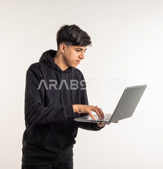 بورتريه شاب مراهق خليجي سعودي يستخدم الابتوب ، يتابع حصص الاونلاين عن طريق الحاسوب المحمول ، التعلم عن بعد ، مفهوم التعليم عبر الانترنت ، التعليم المنزلي ، خلفية بيضاء