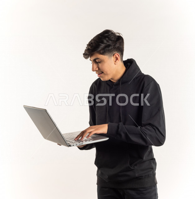 بورتريه شاب مراهق خليجي سعودي يستخدم الابتوب ، يتابع حصص الاونلاين عن طريق الحاسوب المحمول ، التعلم عن بعد ، مفهوم التعليم عبر الانترنت ، التعليم المنزلي ، خلفية بيضاء