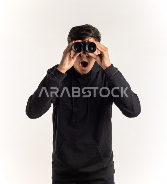 بورتريه شاب مراهق خليجي سعودي يقوم بالنظر من خلال المنظار ثنائي العينين (التلسكوب) , خلفية بيضاء
