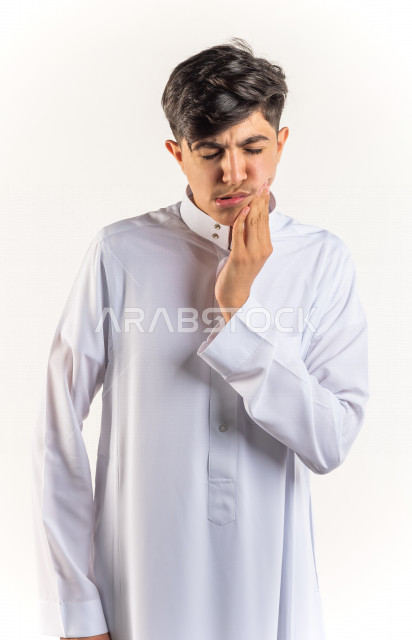 بورتريه شاب مراهق خليجي سعودي مريض بإيماءات وجه ويدين مختلفة تدل على الألم و الوجع في الأسنان ، خلفية بيضاء