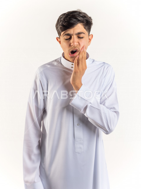 بورتريه شاب مراهق خليجي سعودي مريض بإيماءات وجه ويدين مختلفة تدل على الألم و الوجع في الأسنان ، خلفية بيضاء