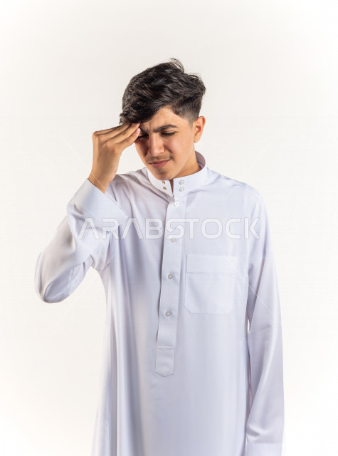 بورتريه شاب مراهق خليجي سعودي مريض يضع يده على رأسه بإيماءات وجه ويدين مختلفة تدل على الألم و الوجع ، خلفية بيضاء