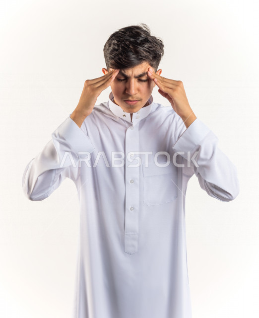 بورتريه شاب مراهق خليجي سعودي مريض يضع يده على رأسه بإيماءات وجه ويدين مختلفة تدل على الألم و الوجع ، خلفية بيضاء