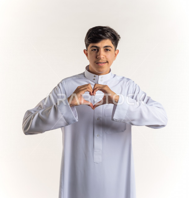 بورتريه شاب مراهق خليجي سعودي يقوم بحركة القلب باليد بإيماءات وجه ويدين مختلفة , خلفية بيضاء