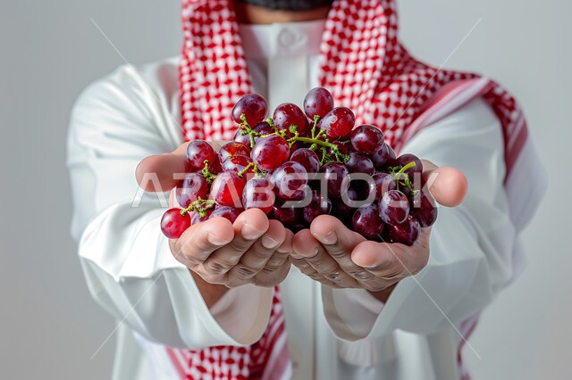 محاصيل زراعية سعودية ذات جودة عالية، تحسين مستويات الطاقة والتركيز خلال اليوم من خلال تناول الفواكه، وجبات دايت صحية خفيفة، بورتريه مقرب لرجل عربي سعودي خليجي يرتدي الشماغ والزي التقليدي يحمل بيده مجموعة من حبات العنب، خلفيه بيضاء