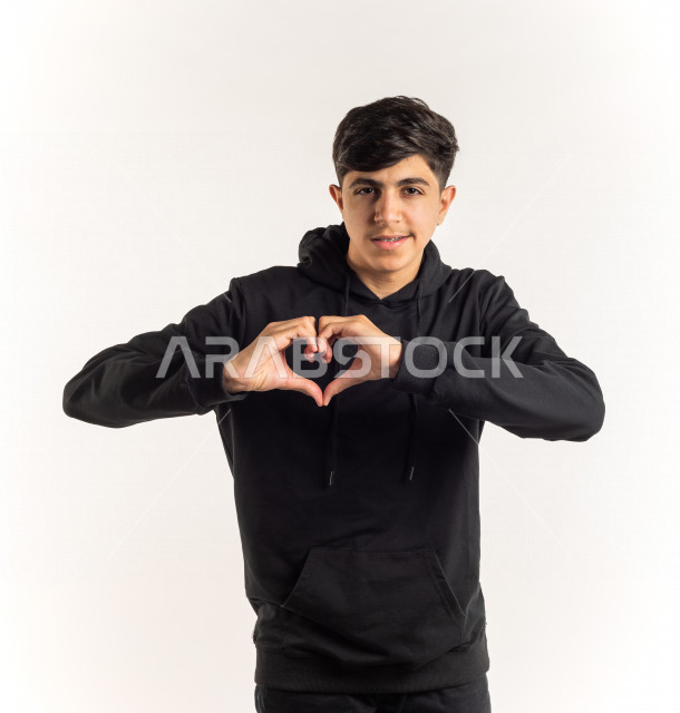 Portrait of a young Saudi Arabian Gulf teenager doing the heart movement by hand with different facial and hands gestures, white background