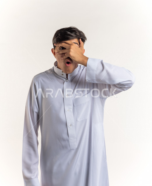 بورتريه شاب مراهق خليجي سعودي مريض يضع يده على رأسه بإيماءات وجه ويدين مختلفة تدل على الألم و الوجع ، خلفية بيضاء