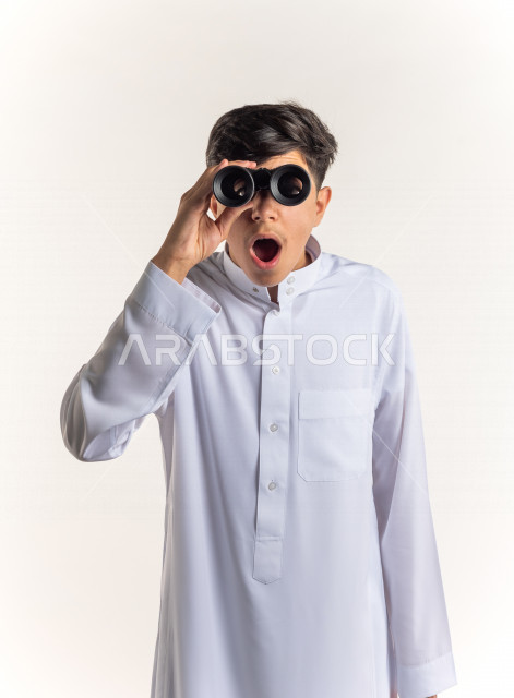 بورتريه شاب مراهق خليجي سعودي يقوم بالنظر من خلال المنظار ثنائي العينين (التلسكوب) , خلفية بيضاء