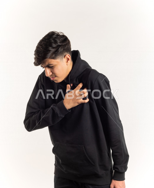 Portrait of a young Saudi Arabian Gulf teenager placing his hand on his chest feeling a state of tingling and pain in his heart, white background