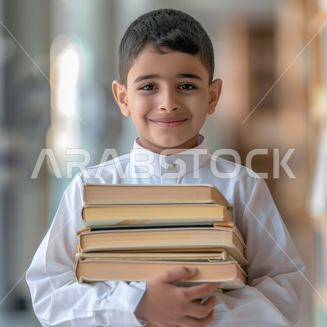 الثقافة والقراءة والإستطلاع، صورة مقربة لطالب عربي خليجي سعودي يرتدي الثوب التقليدي يحمل بيد مجموعة من الكتب، مراجعة الدروس اليومية، التعليم الدراسي في المملكة العربية السعودية