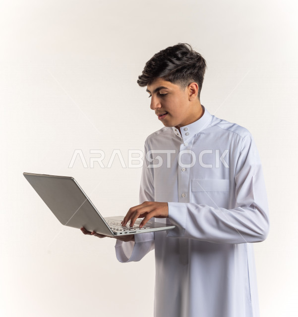 بورتريه شاب مراهق خليجي سعودي يستخدم الابتوب ، يتابع حصص الاونلاين عن طريق الحاسوب المحمول ، التعلم عن بعد ، مفهوم التعليم عبر الانترنت ، التعليم المنزلي ، خلفية بيضاء