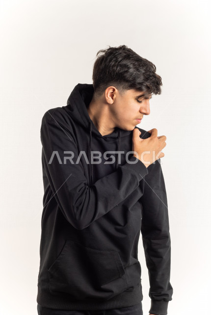 Portrait of a young Saudi Arabian Gulf teenager putting his hand on his shoulder feeling a state of aches and pain with different facial and hands gestures, white background