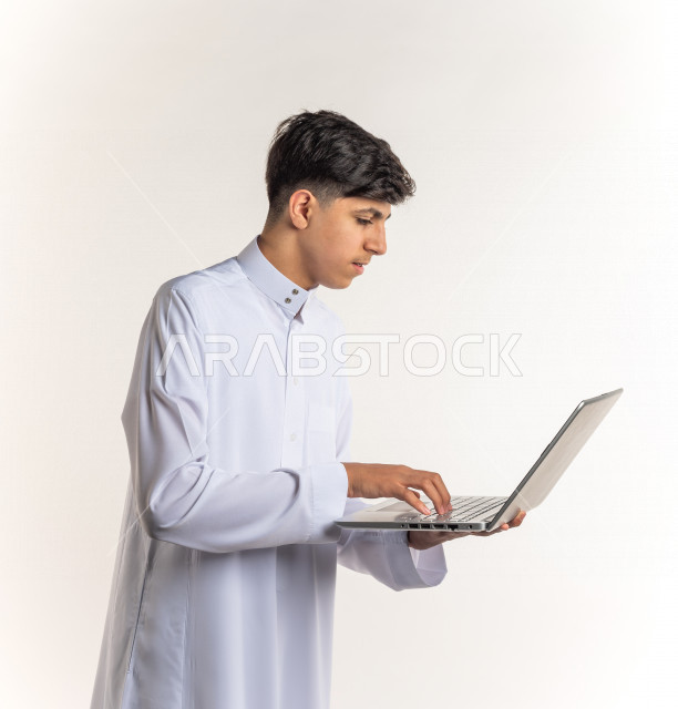 بورتريه شاب مراهق خليجي سعودي يستخدم الابتوب ، يتابع حصص الاونلاين عن طريق الحاسوب المحمول ، التعلم عن بعد ، مفهوم التعليم عبر الانترنت ، التعليم المنزلي ، خلفية بيضاء