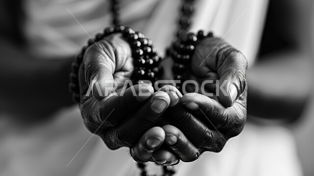 الإكثار من ذكر الله تعالى والإستغفار والدعاء, تصوير مقرب لأيدي رجل عربي سعودي خليجي يرفع يديه يمسك السبحه, مفهوم الإجتهاد في العباده و التقرب الى الله في شهر رمضان المبارك, يوم الجمعه المباركه، خلفيه رمادية