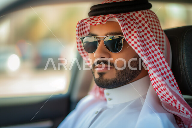 ايماءات الجدية والثقة بالنفس، الاهتمام بالمظهر الخارجي، مفهوم الأناقة والجولة، صورة مقربة لرجل عربي سعودي خليجي يرتدي الزي التقليدي والنظارة الشمسية يجلس بداخل سيارته، وسائل التنقل والمواصلات في السعودية