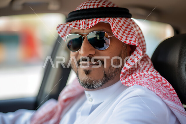 تعابير الجدية والثقة بالنفس، الاهتمام بالمظهر الخارجي، مفهوم الأناقة والجولة، صورة مقربة لرجل عربي سعودي خليجي يرتدي الزي التقليدي والنظارة الشمسية يجلس بداخل سيارته، وسائل التنقل والمواصلات في السعودية