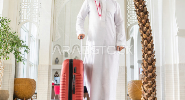 صورة مقربة لرجل أعمال خليجي سعودي يجر حقيبة سفر داخل الفندق , يرتدي ثوب أبيض , سياحة وفندقة , قضاء أوقات ممتعة