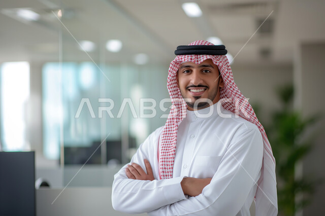 The concept of masculinity and elegance, paying attention to external appearance and representing important figures, a smiling Saudi Gulf Arab young man wearing traditional clothing looking at the camera with gestures of pride and self-confidence, standing happily in the workplace