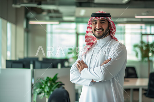 Concern with external appearance and elegance, the concept of masculinity and important figures, a smiling Saudi Gulf Arab young man wearing traditional clothing looking at the camera with gestures of pride and self-confidence, standing happily in the workplace