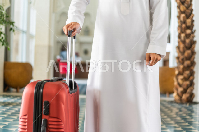 صورة مقربة لرجل أعمال خليجي سعودي يجر حقيبة سفر داخل الفندق , يرتدي ثوب أبيض , سياحة وفندقة , قضاء أوقات ممتعة